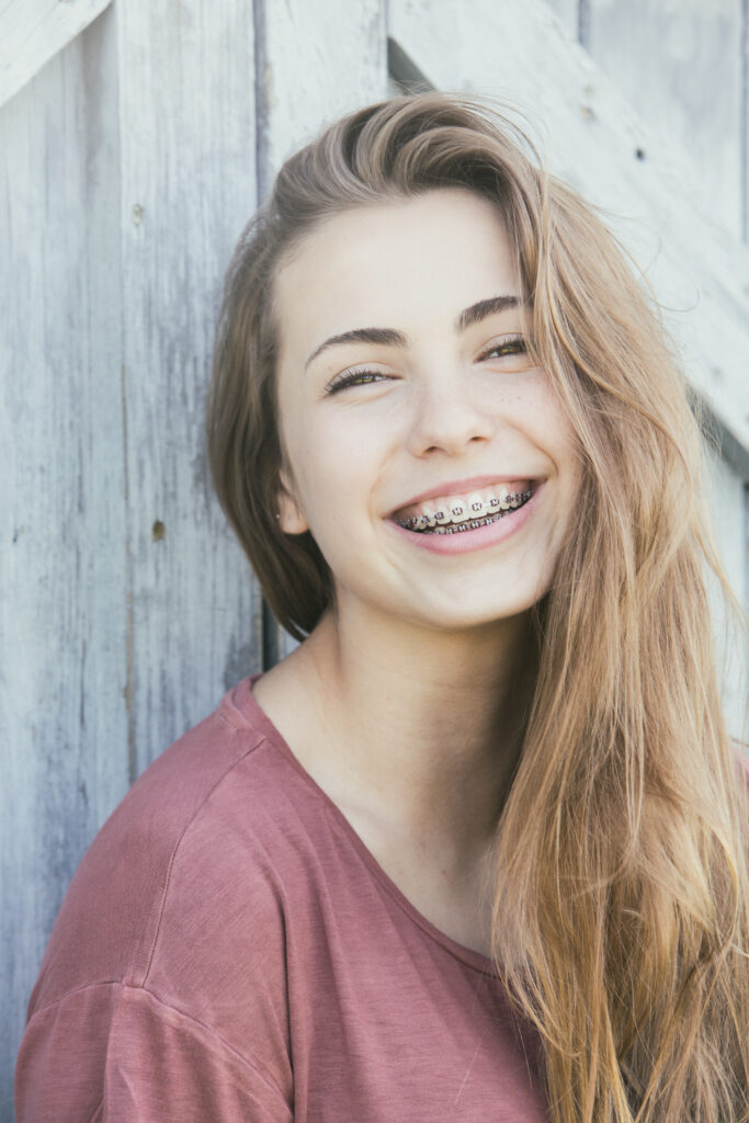 young teenage girl with braces smiling in front of wood door