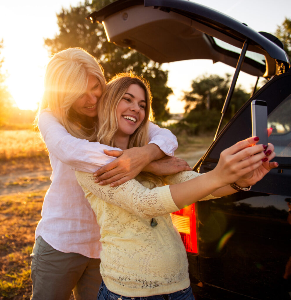 Mom and teen smiling together with car trunk open, taking selfie